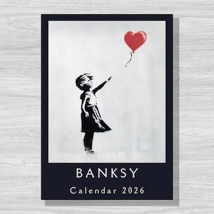 Puede incluir: Calendario con una obra de arte de Banksy. Muestra un esténcil en blanco y negro de un niño que alcanza un globo rojo en forma de corazón. El texto "BANKSY" y "Calendar 2026" están impresos en blanco sobre un fondo azul oscuro.