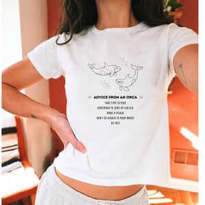 May include: White t-shirt with a black line drawing of two orcas swimming. The text "Advice from an Orca" is printed on the shirt, along with the following advice: "Take time to play, Remember to come up for air, Make a splash, Don't be afraid to make waves, Be free."