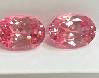 Puede incluir: Dos gemas facetadas de corte ovalado con un vibrante tono rosa. Las gemas se muestran una al lado de la otra, mostrando sus intrincadas estructuras internas y su brillante brillo. Las gemas están sobre un fondo blanco.