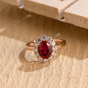 May include: A rose gold ring featuring a large oval ruby set in a halo of smaller diamonds.