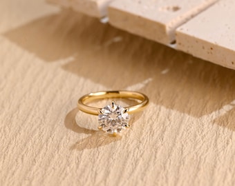 May include: A gold engagement ring with a large, round, clear diamond set in a six-prong setting.