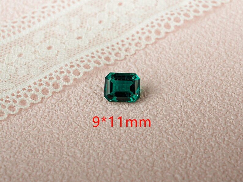 May include: A dark green emerald gemstone with a rectangular cut. The gemstone measures 9 by 11 millimeters.