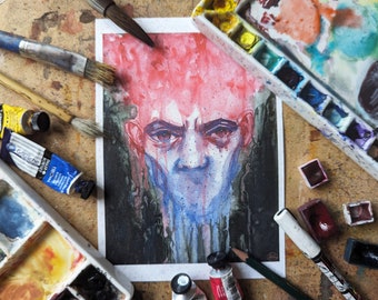 May include: Watercolour painting of a person's face with red hair and blue and purple dripping paint. The painting is on a white background and is surrounded by art supplies.