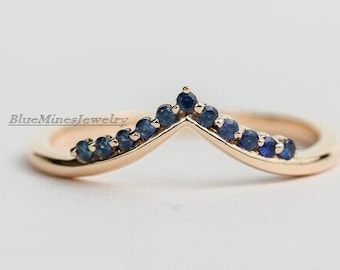 Puede incluir: Un delicado anillo de banda de oro con una fila de pequeños zafiros azules curvada en forma de V.