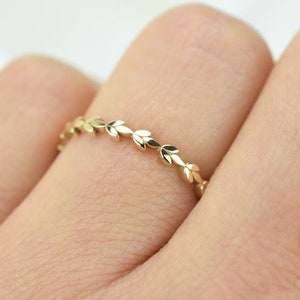 Puede incluir: Un delicado anillo de oro con un diseño de pequeñas hojas alrededor de la banda.