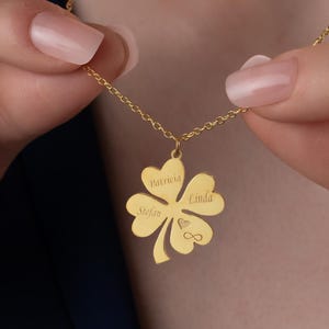 May include: Gold necklace with a four-leaf clover pendant. The pendant has the names "Katrina", "Mike", "Linda", and an infinity symbol engraved on it.