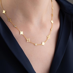 May include: A gold necklace with a delicate chain and small, open flower charms. The necklace is accented with clear, round stones.