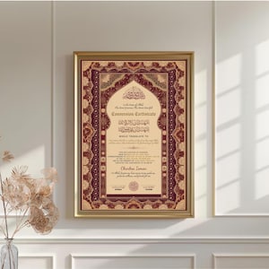 May include: A framed conversion certificate with ornate burgundy and gold detailing. The certificate features Arabic calligraphy and English text, including the name "Charles Iman". The frame is a warm gold color.