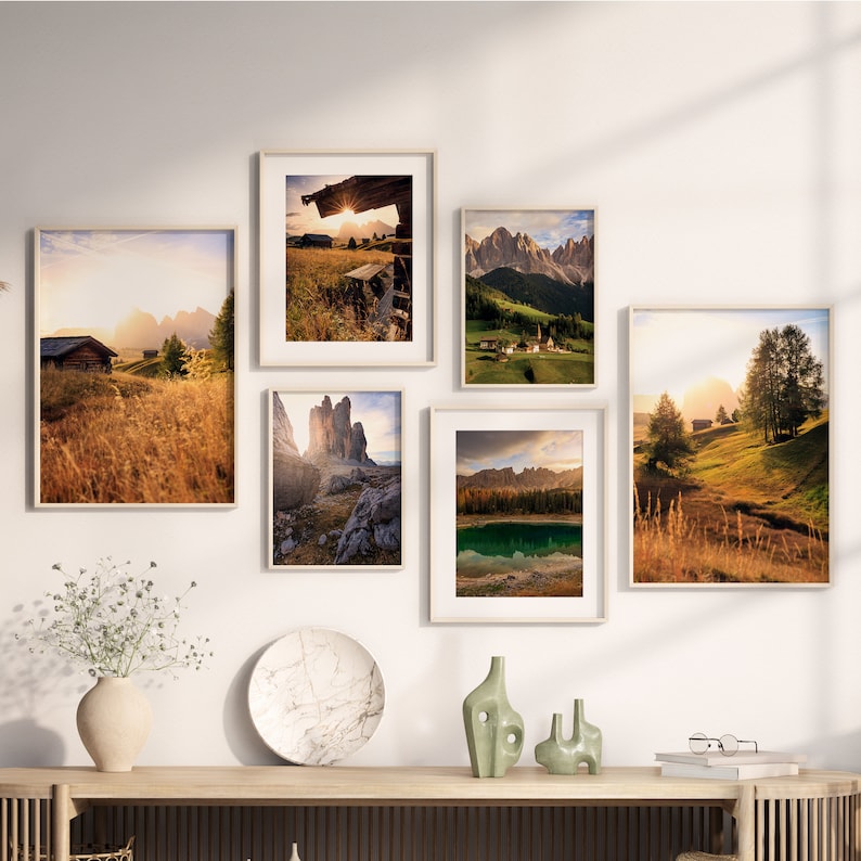May include: A collection of six framed landscape photographs featuring scenic mountain views, golden fields, and a lake. The photos are arranged in a grid pattern on a white wall.