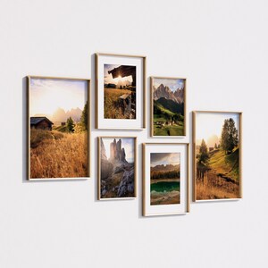 May include: Five framed landscape photographs of mountains, valleys, and forests. The photos are arranged in a grid pattern on a white wall.