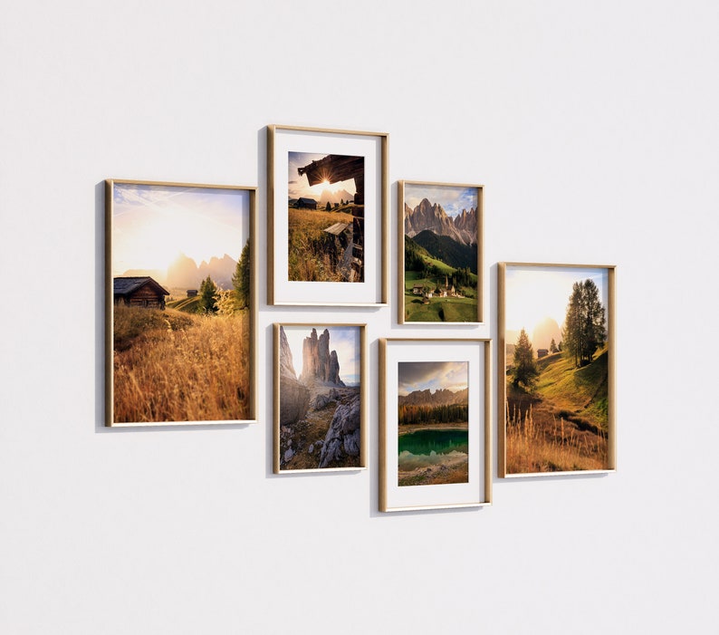 May include: Five framed landscape photographs of mountains, valleys, and forests. The photos are arranged in a grid pattern on a white wall.