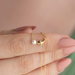 May include: A delicate gold chain necklace with a small pearl and a dolphin charm.