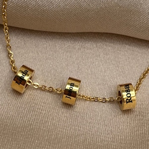 May include: Gold chain necklace with three round charms, each engraved with a name: Linda, Jason, and Rosa.