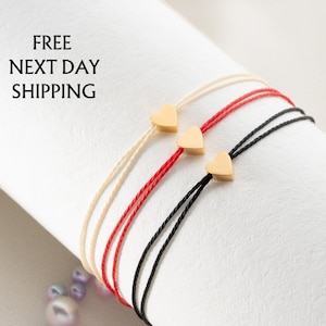 May include: Three friendship bracelets with gold heart charms. The bracelets are red, black, and cream.