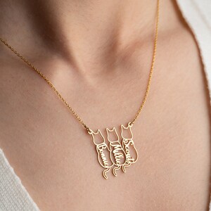 Op de afbeelding: Gouden ketting met drie katten-silhouetten, elk met een gegraveerde naam: Bonnie, Millie en Scout.