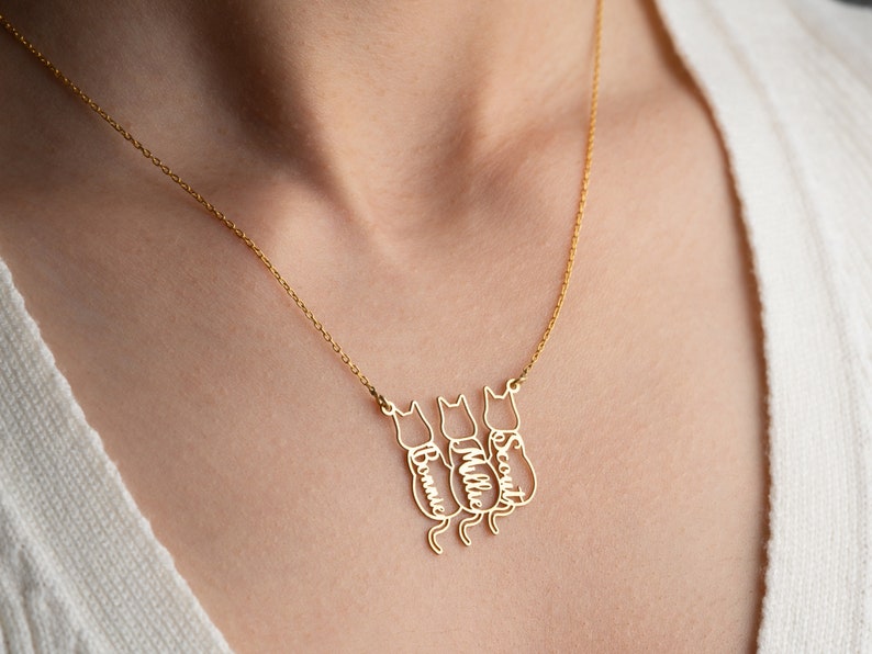 Op de afbeelding: Gouden ketting met drie katten-silhouetten, elk met een gegraveerde naam: Bonnie, Millie en Scout.