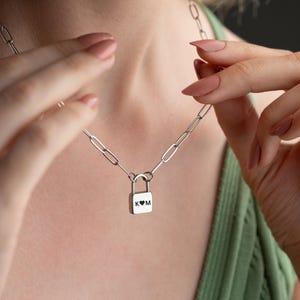 以下が含まれることがあります： 鍵の形をしたペンダントがついたシルバーチェーンネックレス。ペンダントには「K」と「M」の文字が刻まれており、その間にハートマークがあります。
