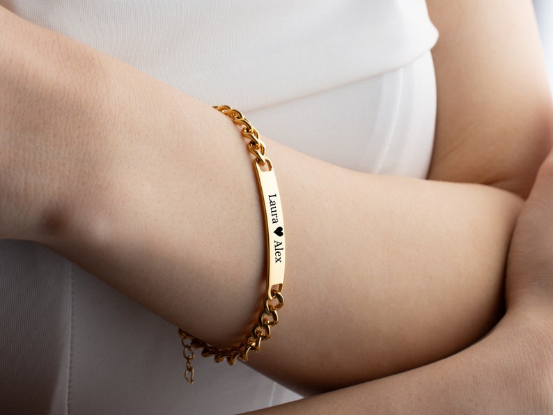 May include: Gold chain bracelet with a personalized nameplate that reads "Laura &hearts; Alex".