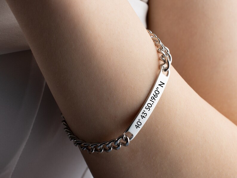 May include: Silver chain bracelet with a rectangular tag engraved with the coordinates "40&deg; 43' 50.1960" N.