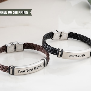 May include: Two leather bracelets with metal clasps and engraved metal plates. One bracelet is brown and has the text "Your Text Here" engraved on the plate. The other bracelet is black and has the date "08.07.2015" engraved on the plate.