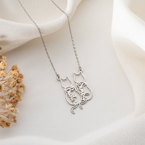 Op de afbeelding: Zilveren ketting met twee katten-silhouetten, elk met een naam erin gegraveerd: "Buster" en "Simba".