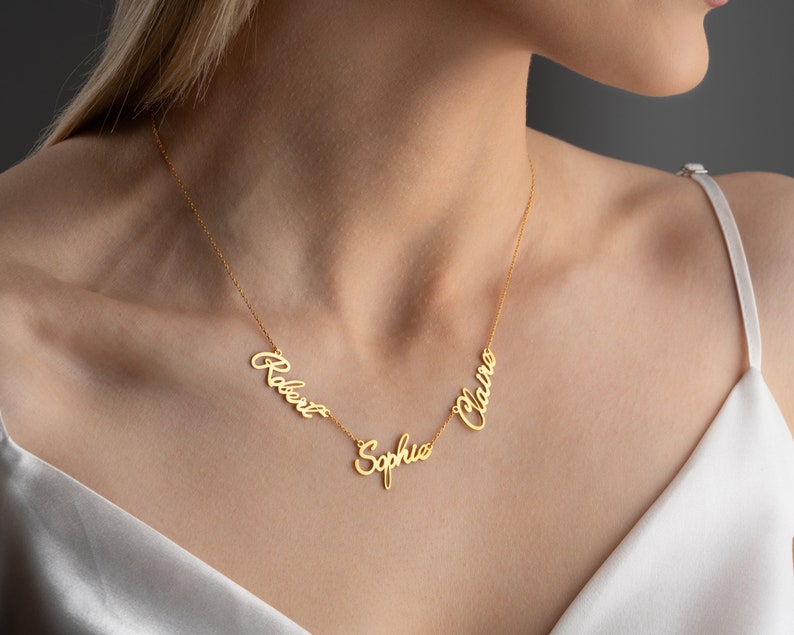 May include: Gold necklace with three names, "Robert", "Sophia", and "Claire", written in a cursive script.