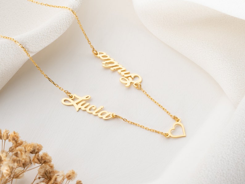 May include: Gold necklace with two names, "Lucia" and "Emma", and a heart charm.