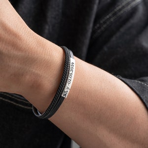 May include: A black leather bracelet with a silver plate engraved with the date "21-02-2019".