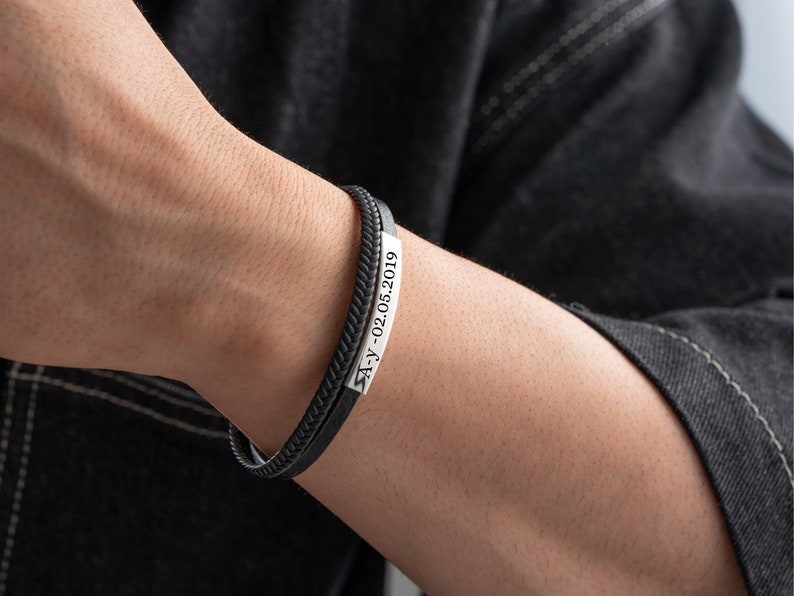 May include: A black leather bracelet with a silver plate engraved with the date "21-02-2019".
