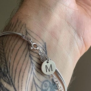 May include: A silver chain bracelet with a silver charm that has the letter "M" engraved on it.
