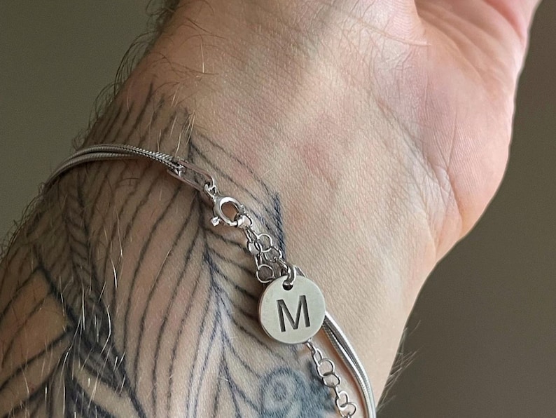 May include: A silver chain bracelet with a silver charm that has the letter "M" engraved on it.