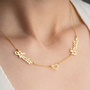 May include: Gold necklace with two names, "Lucia" and "Emilia", separated by a heart charm.