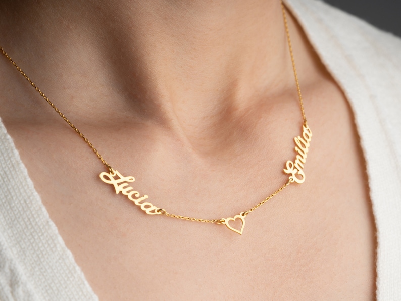 May include: Gold necklace with two names, "Lucia" and "Emilia", separated by a heart charm.