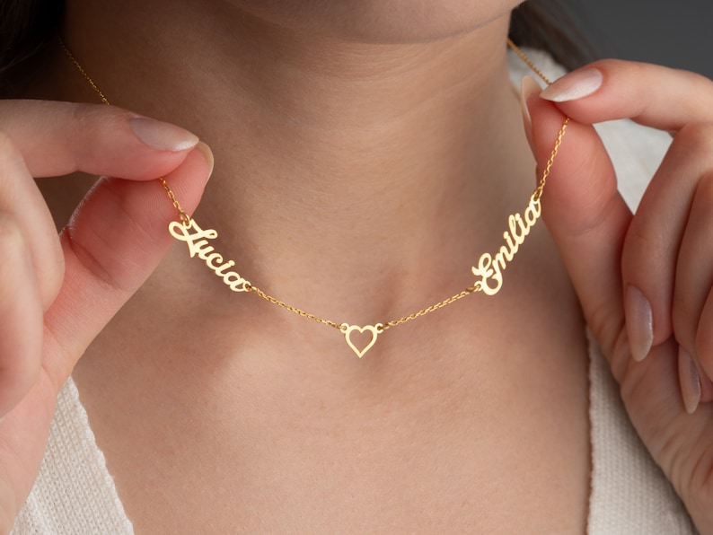 May include: Gold necklace with two names, "Lucia" and "Emilia", separated by a small heart charm.