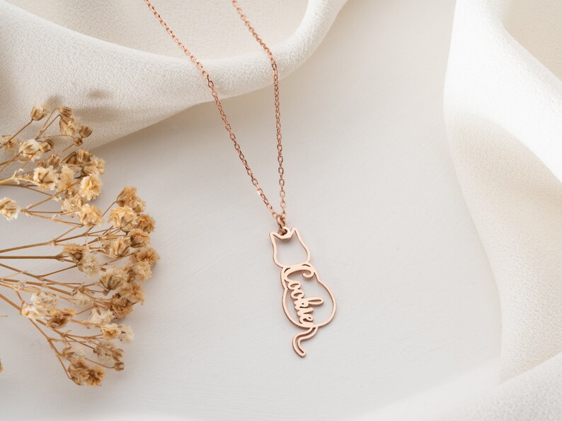 Op de afbeelding: Roze gouden ketting met een hanger in de vorm van een katten silhouet. De hanger heeft de naam "Cookie" geschreven in het lichaam van de kat.