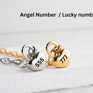 以下が含まれることがあります： 555と777が刻まれた、銀と金のハート型の鍵のチャームが2つ。チャームは銀のチェーンに繋がっています。