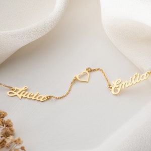 May include: Gold necklace with two names, "Lucia" and "Emilia", connected by a small heart charm.