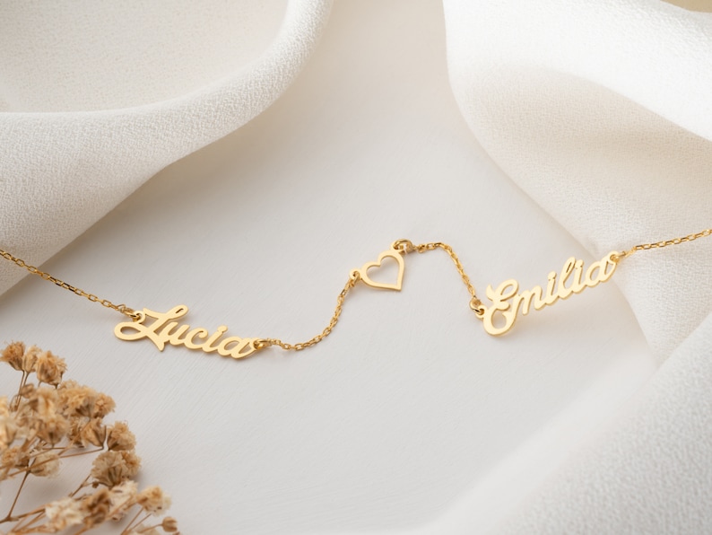 May include: Gold necklace with two names, "Lucia" and "Emilia", connected by a small heart charm.