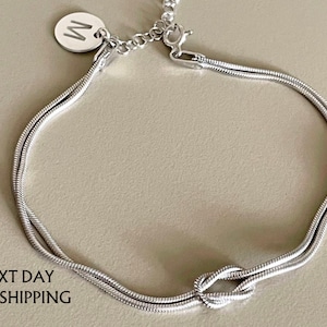 May include: A silver chain bracelet with a knot design and a small silver charm with the letter "W" on it.