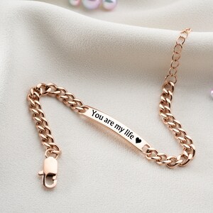 May include: A rose gold chain bracelet with a small rectangular tag that reads "You are my life" with a heart symbol.