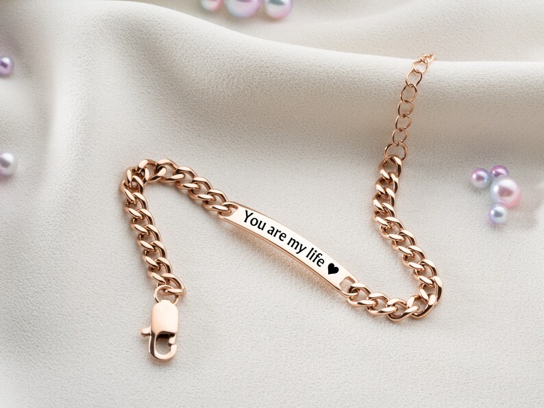 May include: A rose gold chain bracelet with a small rectangular tag that reads "You are my life" with a heart symbol.