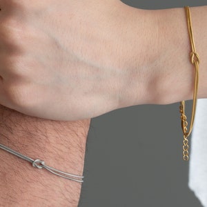 May include: Two matching bracelets with a knot design. One bracelet is silver and the other is gold.