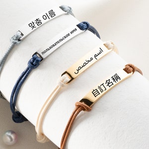 May include: Four bracelets with adjustable cords and personalized nameplates. The nameplates are silver, gold, and two different shades of silver. The nameplates are engraved with the names "멋좀 이쁨", "пользовательское имя", "اسم  مُصطفى", and "自訂名稱".