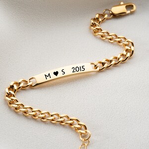 May include: Gold chain bracelet with a personalized bar charm engraved with the letters "M", a heart symbol, "S", and the year "2015".