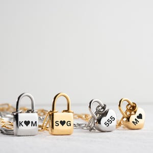 May include: Four gold and silver lockets with chains. The lockets are engraved with the letters "K ♥ M", "S ♥ G", "555", and "M".