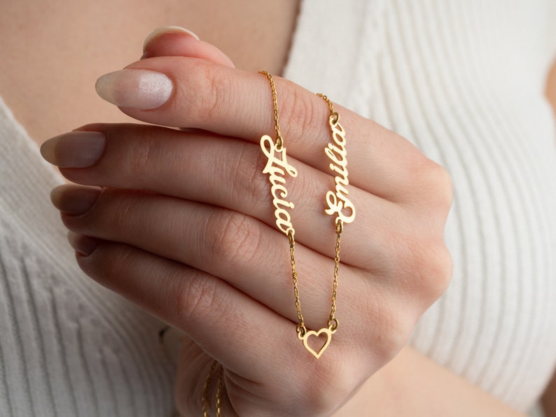 May include: Gold necklace with two nameplates, "Lucia" and "Emilia", and a small heart charm.