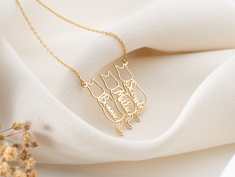 Op de afbeelding: Gouden ketting met drie katten-silhouetten, elk met een gegraveerde naam: Bonnie, Millie en Scout.