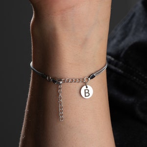 May include: A silver bracelet with a black cord and a silver charm with the letter "B" on it.