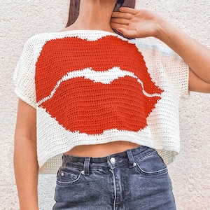 May include: Crocheted white top featuring a large red lip design. The short-sleeved top is made of a textured yarn and has a cropped fit. The lip design is centered on the front of the top.