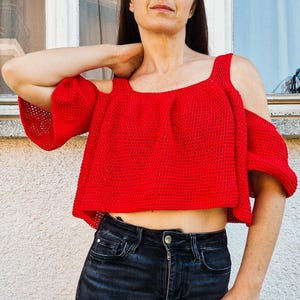 May include: A red crochet top with a cold shoulder design and short sleeves. The top is cropped and has a loose fit.